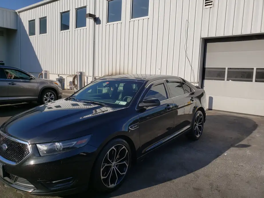 Black Ford sedan parked outside a metal-sided shop after a full detail, paint clean and glossy