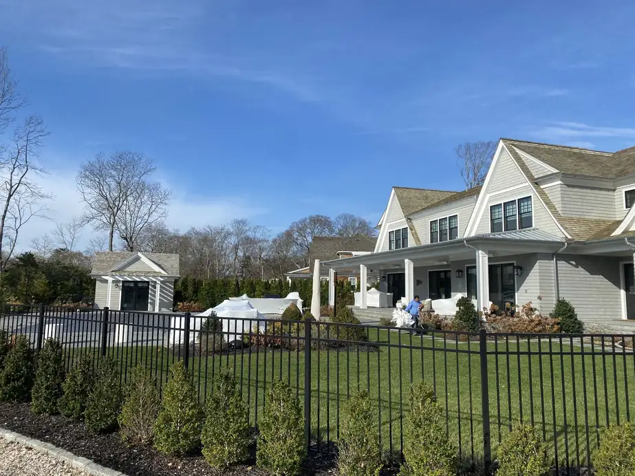 Large shingled house with shrink-wrapped patio furniture on the lawn