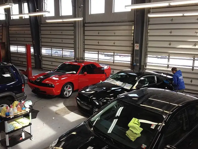 Red and black muscle cars in the shop bay while a detailer works on a coating