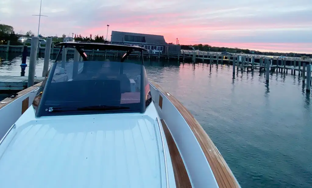 Bow of a white and teak powerboat at a marina slip at pink dusk